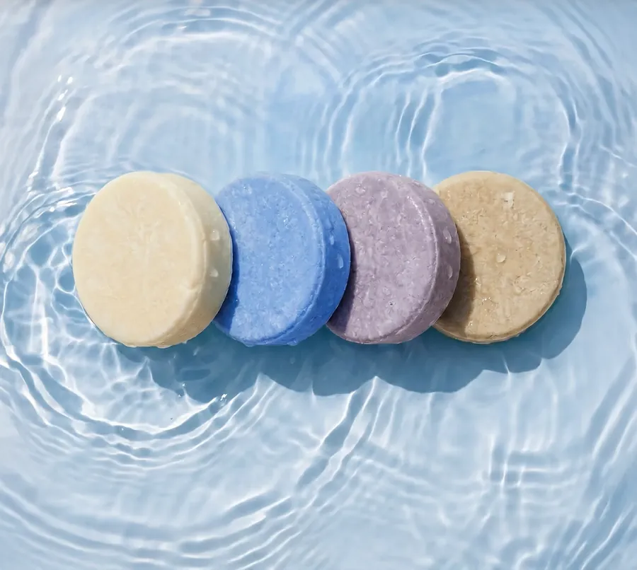 Four round shampoo bars resting in sunlit rippling water