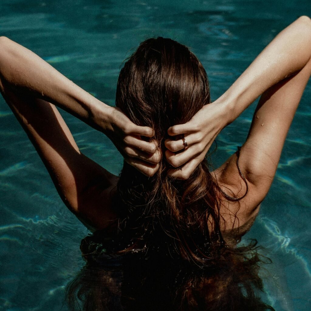 A peaceful back view of a woman in a swimming pool, hands touching her hair, creating a tranquil mood.