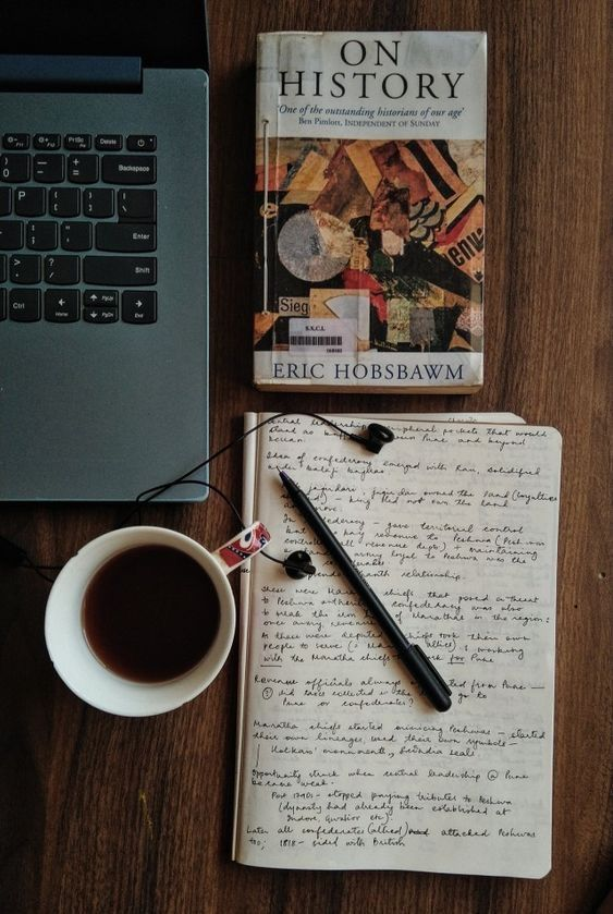 A laptop closed beside an open notebook, a pen, and a coffee on a wooden desk