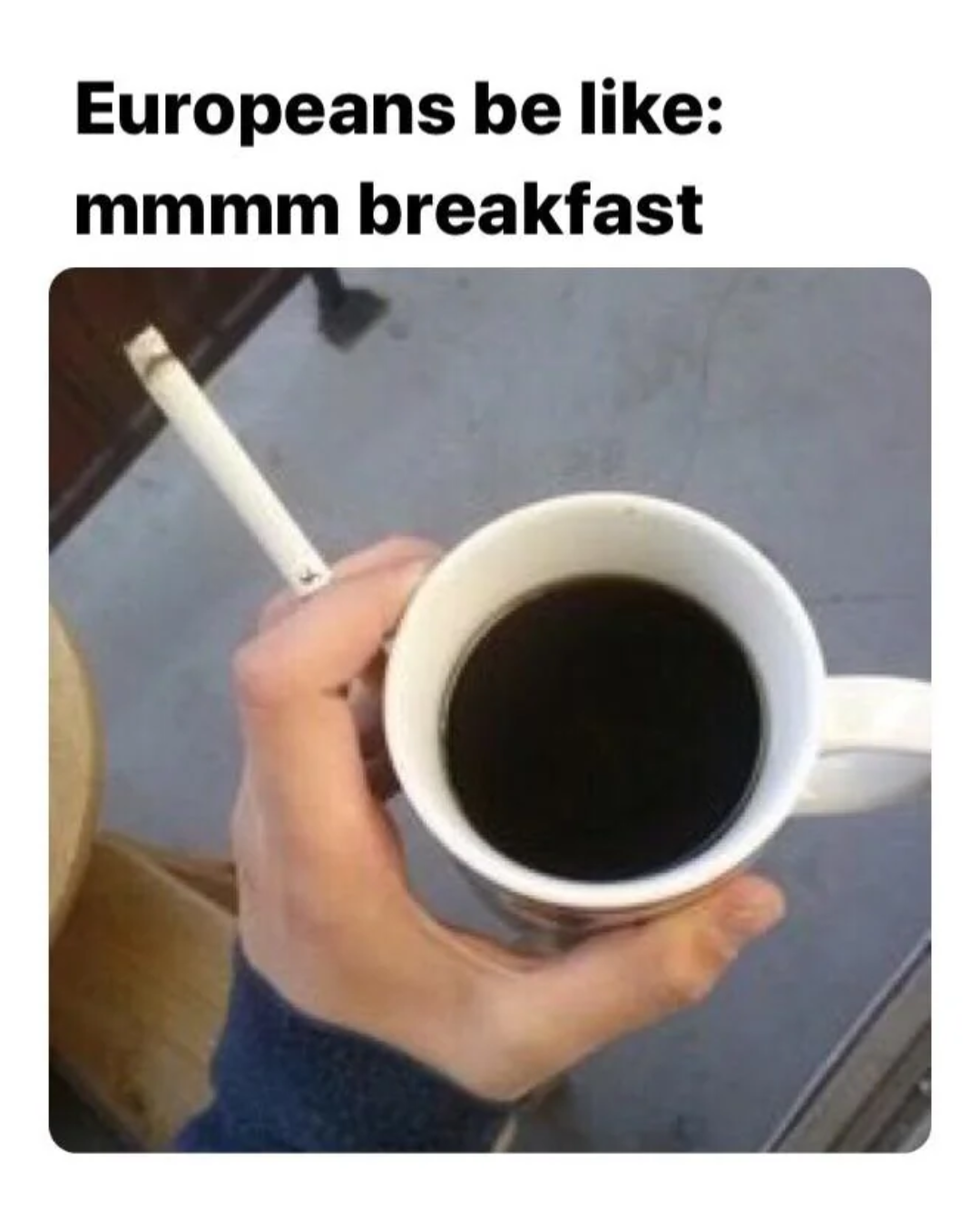 Meme: Europeans be like: mmmm breakfast — a hand holds a white mug of black coffee alongside a lit cigarette between the fingers