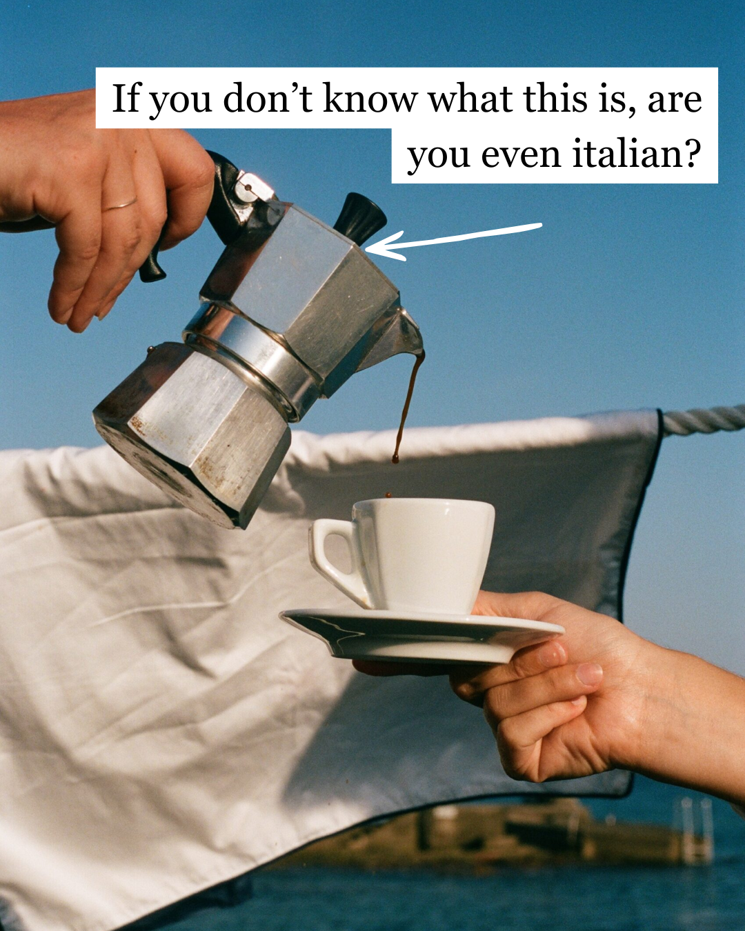 A Bialetti moka pot being poured into a small espresso cup held on a saucer against a bright blue sky near the sea — If you don't know what this is, are you even Italian?